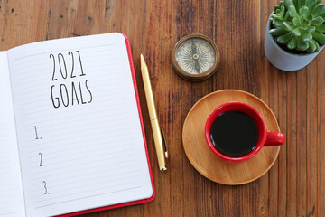 Business concept of top view 2021 goals list with notebook, cup of coffee over wooden desk
