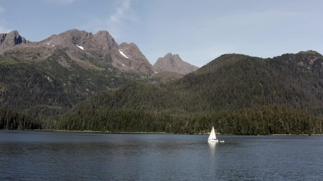 Solitary Sailboat Sailing In Sea with Scenic View Of Mountains And Forest In Alaska USA - panning wide shot