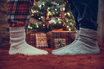 Woman feet standing in tip toe in winter socks on male lags on a fluffy red blanket near a...