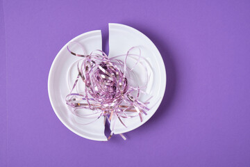 shiny festive tinsel on broken white plate, purple background