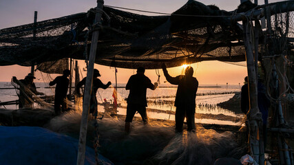 Obraz na płótnie Canvas Fishermen pull fishing net to get fish at sunset