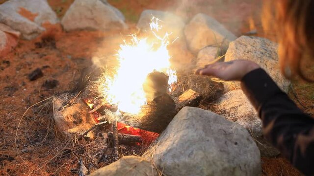 Selective focus of male hands blowing charcoal staff in sparkling bonfire while preparing for fire jamming event in forest in Canada