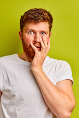 portrait of shocked caucasian male looking at camera at a loss, emotional guy with beard with hands on face, isolated over green background