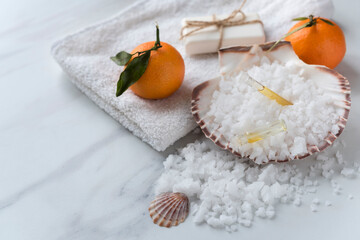 Spa relax concept. Sea shell full of bath salt with vials of oil, towel, soap and two mandarins on...