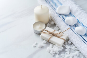 Spa wellness relax concept. Soap, sea salt, candles,  white stones, towel on the light marble background. Copy space