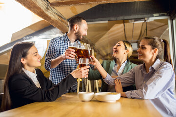 Clinking. Happy co-workers celebrating corporate event after tensioned work day. Look delighted, friendly, cheerful. Drinking beer. Concept of office culture, teamwork, friendship, holidays, weekend.