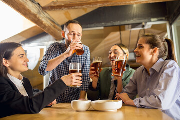 Laughting. Happy co-workers celebrating corporate event after tensioned work day. Look delighted, friendly, cheerful. Drinking beer. Concept of office culture, teamwork, friendship, holidays, weekend.