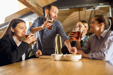 Laughting. Happy co-workers celebrating corporate event after tensioned work day. Look delighted, friendly, cheerful. Drinking beer. Concept of office culture, teamwork, friendship, holidays, weekend.