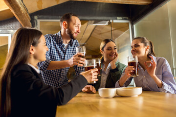 Laughting. Happy co-workers celebrating corporate event after tensioned work day. Look delighted, friendly, cheerful. Drinking beer. Concept of office culture, teamwork, friendship, holidays, weekend.