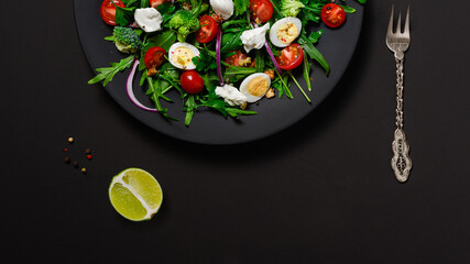salad with arugula, broccoli, cream cheese, cherry tomatoes and walnuts, seasoned with olive oil. Dish on a black matte plate. Copy space below, flat lay