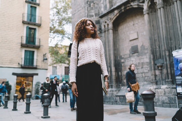 Fototapeta na wymiar Beautiful african american hipster girl traveler in trendy wear explore location and destinations in city, charming dark skinned woman 20s looking at town and architecture on leisure in town