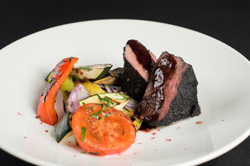 veal tenderloin in ashes with grilled vegetables on a white plate