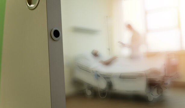 The blur photo of patient lies on a bed in a hospital ward while he is examined by a doctor in protective clothing and a mask.