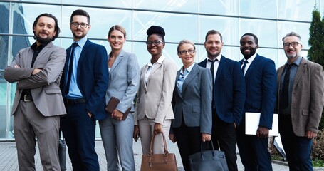 Obraz premium Portrait of mixed-races businessmen and businesswomen standing together outdoors and smiling to camera. Multi ethnic team of business males and females partners. International group of investors.