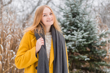 Happy young woman wearing a coat and scarf smiling over nature background, trendy color of year...