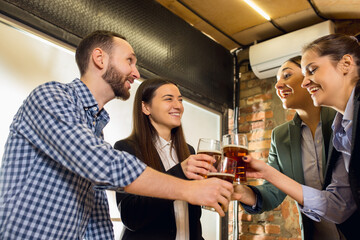 Clinking. Happy co-workers celebrating corporate event after tensioned work day. Look delighted, friendly, cheerful. Drinking beer. Concept of office culture, teamwork, friendship, holidays, weekend.