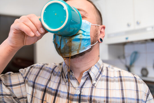 Coronavirus craziness. Close up shot of a man drinking his coffee through a covid protective face mask, making a mess and spilling it over his chest