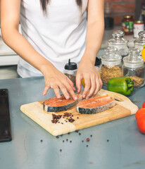 The chef prepares fresh salmon fish on wooden cutting board, fresh salmon slice, sprinkles with spices and Provencal herbs with ingredients. cooking fish food.Cooking vegan cuisine.