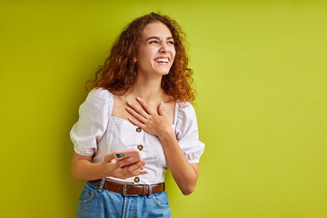 cute curly teen girl enjoy chatting with someone using mobile phone, adorable positive girl in blouse hold phone in hands, smile, isolated on green background in studio