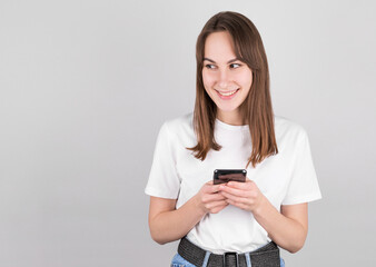 Photo of cheerful cute beautiful young woman chatting by mobile phone isolated over white wall. Looking aside to copyspace.