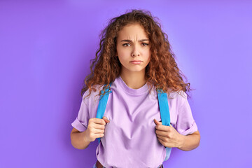 sad upset caucasian terrified girl with school bag looking at camera, unhappy that holidays are finished, isolated purple background