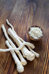 Fresh and grated horseradish root on a wooden background.