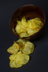 Chips on a black background. Unhealthy food. Crispy potato chips spilled out of the cup