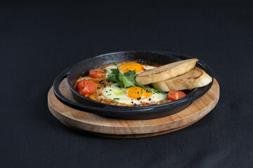 healthy breakfast shakshuka - fried eggs, onion, bell pepper, tomatoes and spices in cast iron stewpan on old wooden plank.