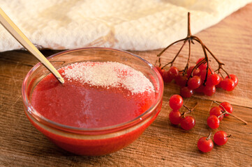 Red berries of a viburnum ground with sugar in a glass vase on a wooden table.