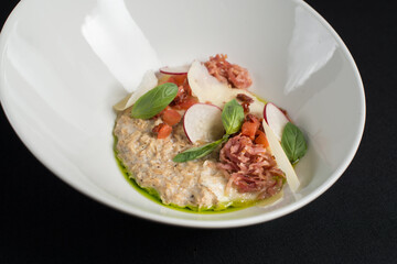 Delicious salted oatmeal, bacon and vegetables on a black tablecloth