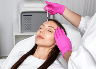 Cosmetologist makes rejuvenating anti wrinkle injections on the face of a beautiful brunette woman....