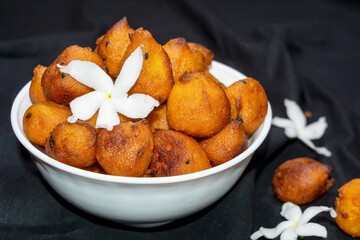 Sugar palm fritters or taler bora in a white bowl on black cloth texture background with white crepe jasmine flower.