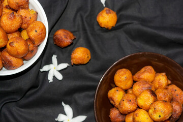 Sugar palm fritters or taler bora in a brown plate on black cloth texture background with white crepe jasmine flower.