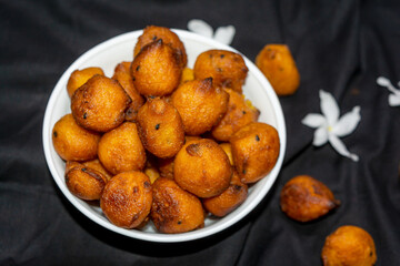 Sugar palm fritters or taler bora in a white bowl on black cloth texture background with white crepe jasmine flower.