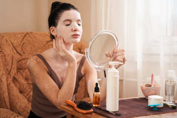 Woman holding little mirror applying a facial mask