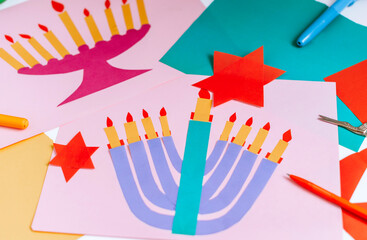 a girl makes a card for happy Hanukkah with her hands, a candelabra and candles on the card