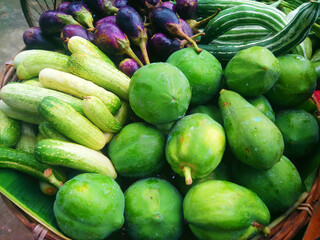Heap of fresh brinjal or eggplant, cucumber and papaya vegetables in a wicker basket for selling on the market.