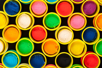 Abstract background from colorful containers of pastel colored play dough on black background. Graphic, artistic.