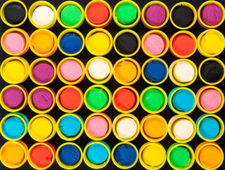 Abstract background from colorful containers of pastel colored play dough on black background. Graphic, artistic.