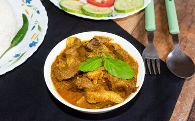 Traditional homemade Bengali style spicy dish mutton curry or lamb curry in a white bowl with rice and salad on wooden background.