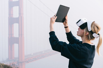 Astonished female in VR glasses with tablet near Golden Gate