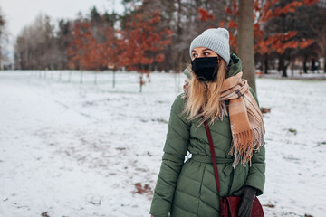 Stylish woman walking in snowy winter park wearing reusable mask during coronavirus covid-19 pandemic.