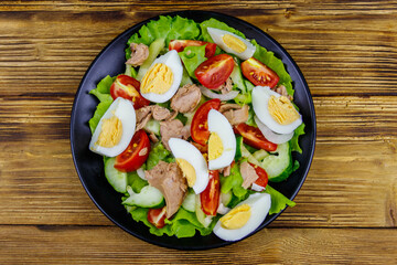 Tasty tuna salad with eggs, lettuce and fresh vegetables on wooden table. Top view
