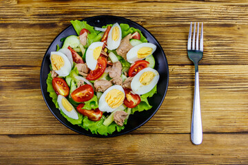 Tasty tuna salad with eggs, lettuce and fresh vegetables on wooden table. Top view