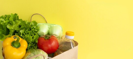 Healthy food delivery during coronavirus. Food donation on yellow background in paper bag package. Help cardboard box wiht various canned food, cereals, pasta and vegetables.