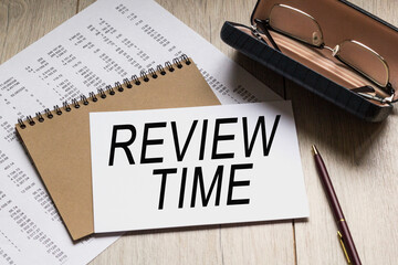 Text REWIEW TIME on a business card lying on a notepad with eyeglasses and text documents. Could be for business, financial and marketing concepts