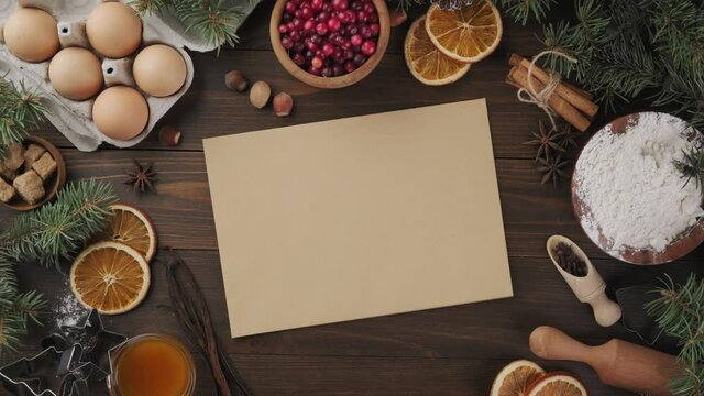Holiday baking background, top-down view. Male hand puts a sheet of craft paper for a recipe on a wooden table. Baking ingredients. Gingerbread cookie recipe. Holiday mood.