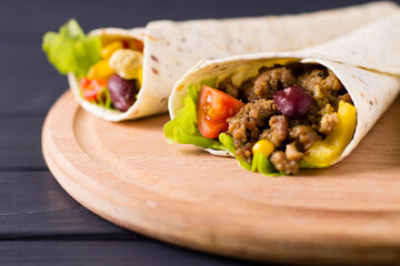 Burrito with beef, chicken, lime, pepper and vegetables, on a wooden board. Mexican food.