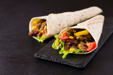 Burrito with beef, chicken, lime, pepper and vegetables, on a stone board. Grey background. Mexican food.