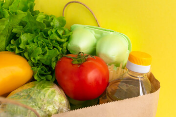 Healthy food delivery during coronavirus. Food donation on yellow background in paper bag package. Help cardboard box wiht various canned food, cereals, pasta and vegetables.